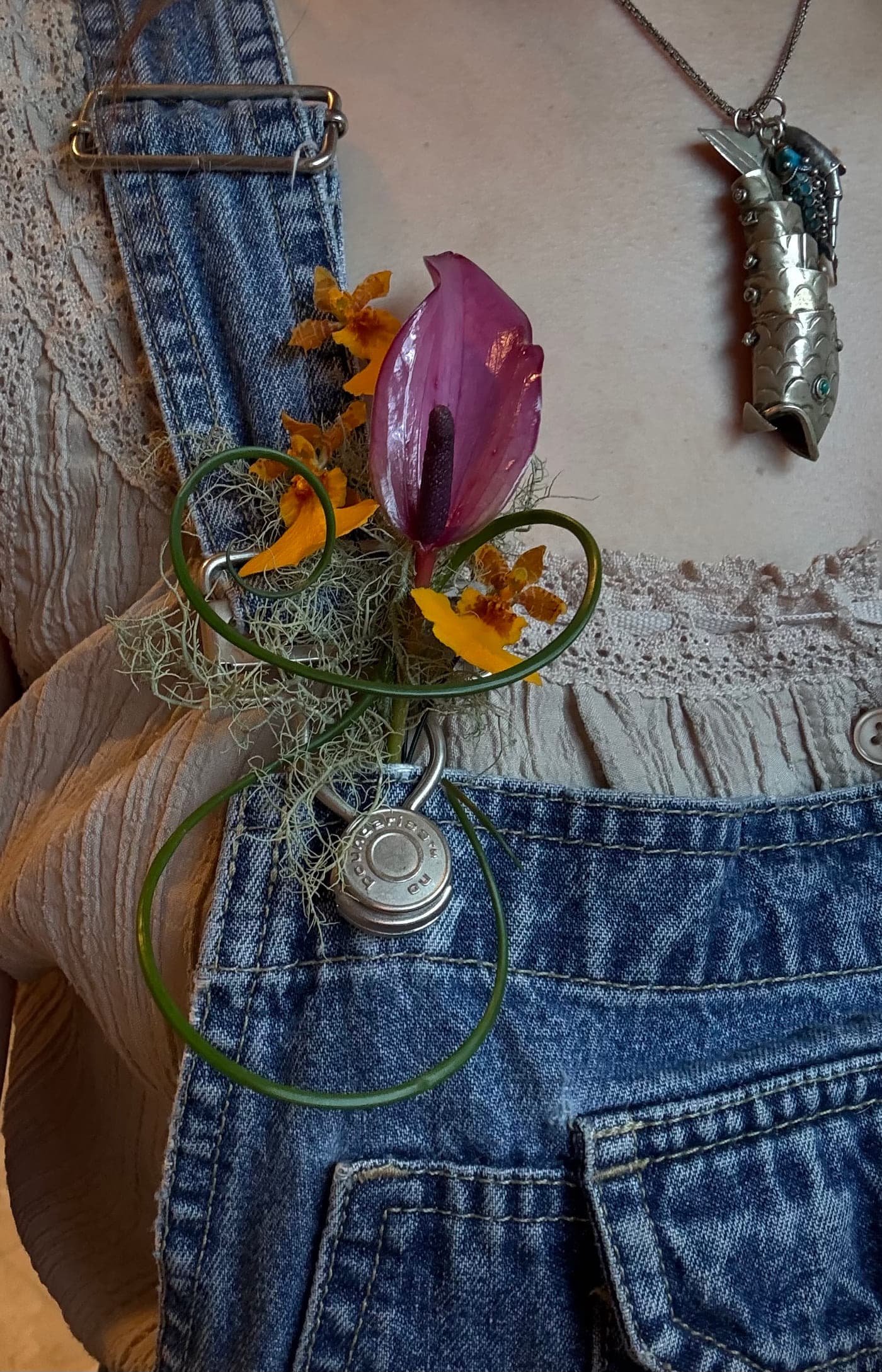A corsage of pink anthurium, oncidium orchid and looped lily grass pinned to denim overalls