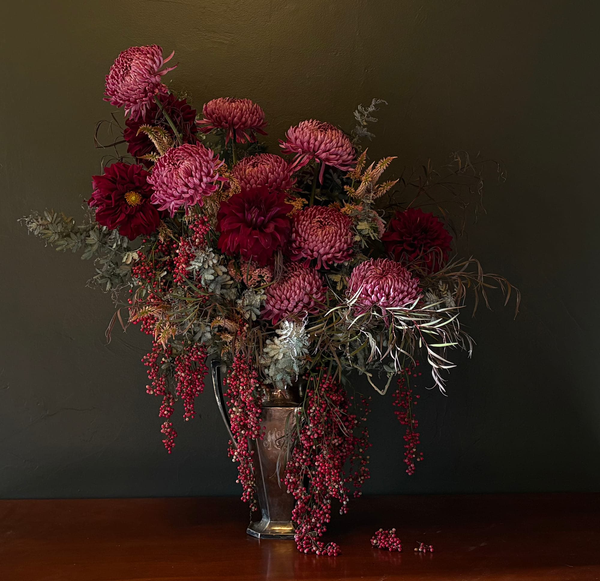 Burgundy and rose chrysanthemums with trailing pepperberry in a silver urn