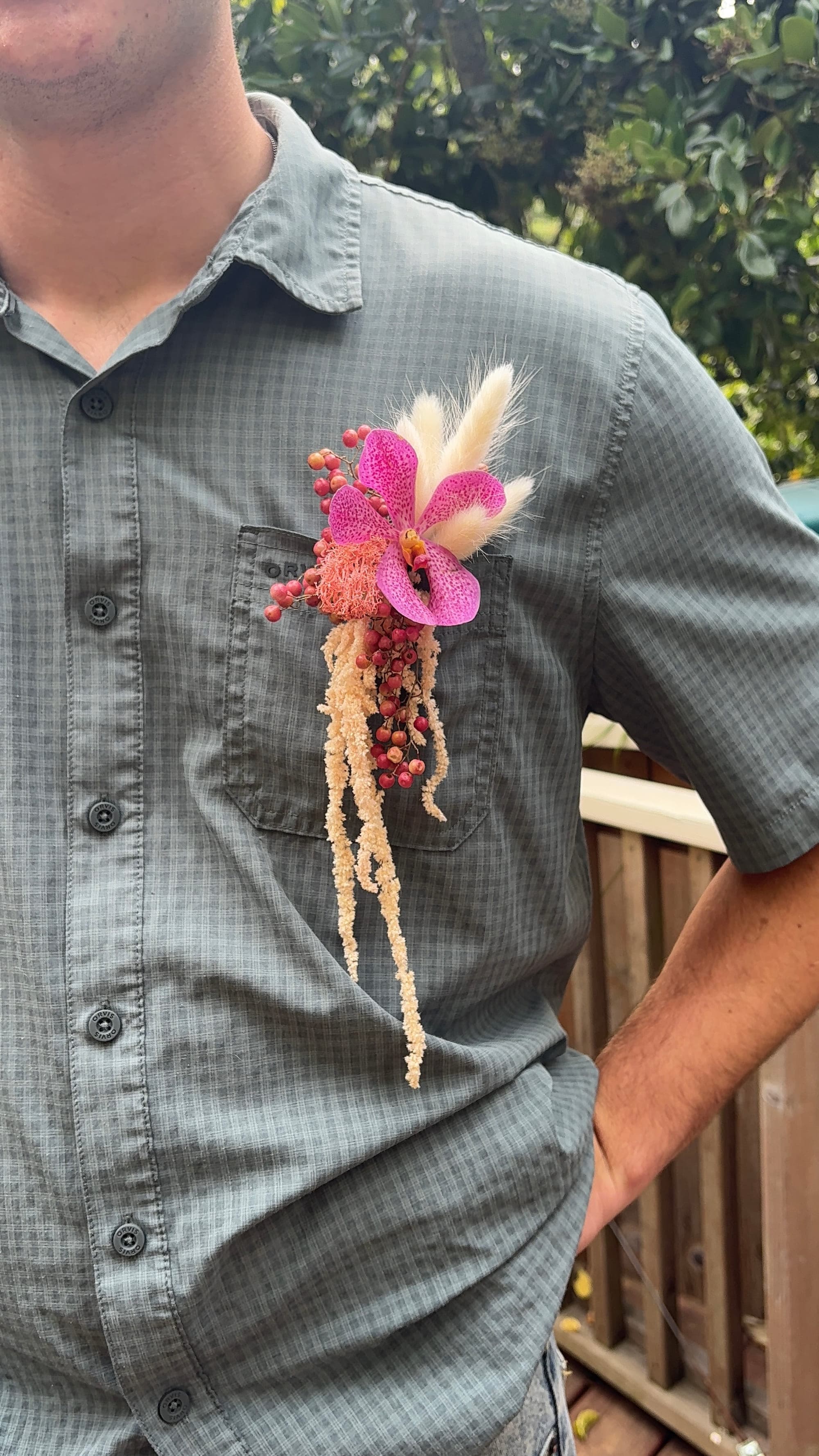 Boutonnière of magenta vanda orchid, bunny tails and pepperberry on a grey shirt
